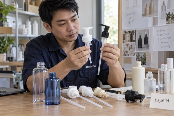 Asian sample reviewer inspecting DayMild soap dispensers: pump-formulation compatibility and variant identity