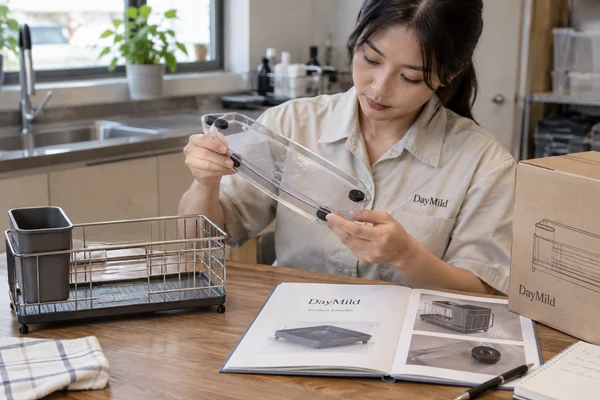 Asian sample reviewer inspecting DayMild sink organizers: drain path, loaded stability and cleaning access